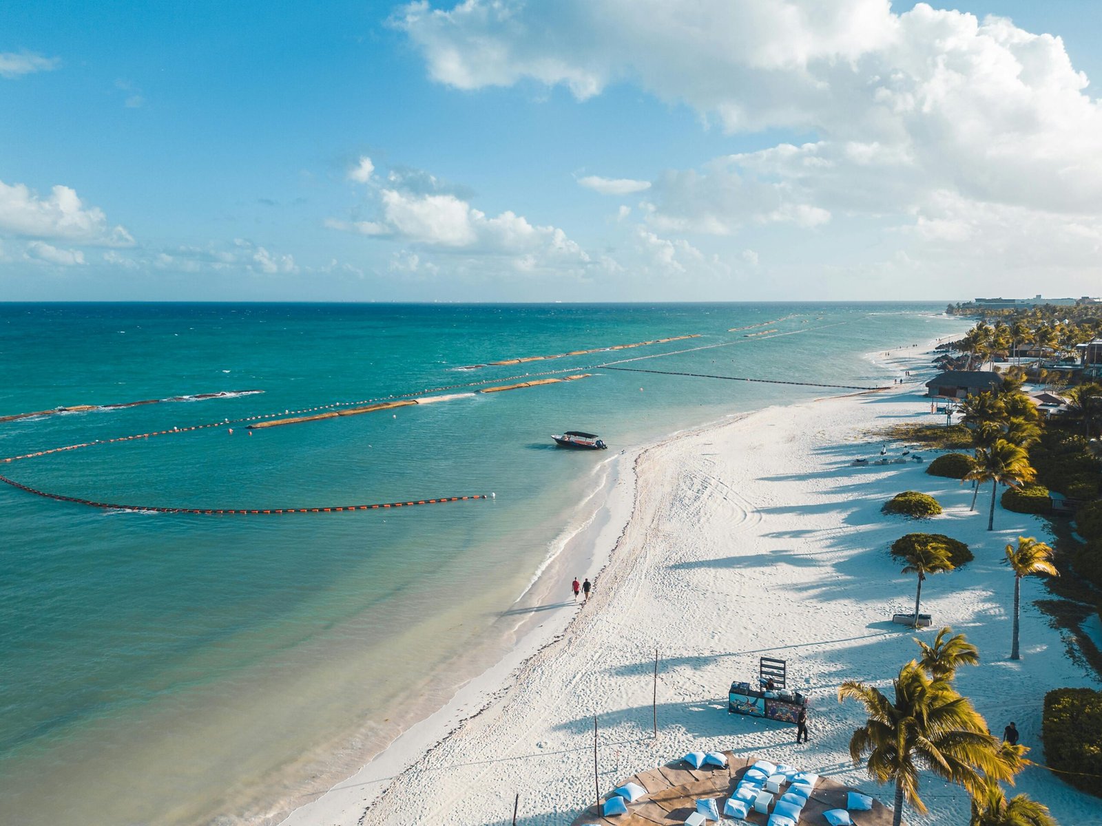 A beautiful aerial view of Playa del Carmen's white sandy beach with clear blue waters and palm trees swaying in the tropical breeze.